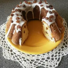 Pyszna babka drożdżowa Ani gotuje, polana lukrem i posypana rodzynkami, na żółtym talerzu.