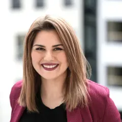Lächelnde junge Frau mit braunen Haaren, die einen pinken Blazer trägt. Sie studiert IU Master Wirtschaftsinformatik und blickt optimistisch in die Zukunft.