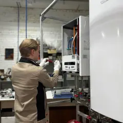 Technik montuje elementy instalacji inteligentny dom, pracując przy białym urządzeniu z rurkami i zaworami.