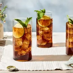 Trzy szklanki orzeźwiającego whisky z colą, ozdobione plasterkami limonki i listkami mięty, stoją na białym obrusie.