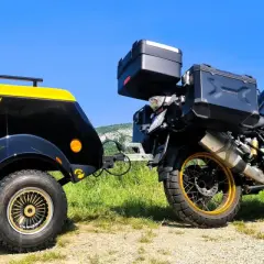 Une remorque pour chien moto, noire et jaune, est attelée à une moto BMW tout-terrain, prête pour une aventure en plein air.