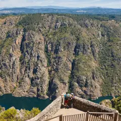 Dos excursionistas contemplan la majestuosidad de los ríos de Galicia, serpenteando entre cañones rocosos y bosques frondosos.