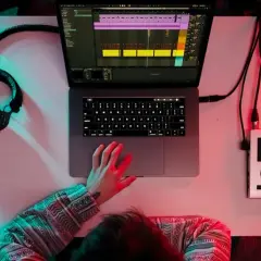 Person am Schreibtisch mit Kopfhörern, Laptop und Audio-Interface. Musikproduktion in 24 bit 48 khz.