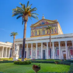 Giardino curato davanti alla Basilica San Paolo, con palme alte e statue.