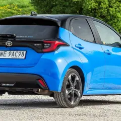 Niebieski Toyota Yaris IV z czarnym dachem, zaparkowany na żwirowej drodze, z zielonym tłem.