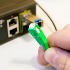 Dłoń trzyma zieloną wtyczkę światłowodową. Obok widać przełącznik Ethernet. Tak sprawdzisz, czy jest światłowód.