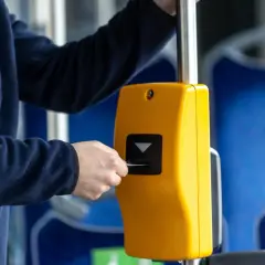 Osoba wkłada kartę do żółtego kasownika w autobusie, pokazując, jak kupić bilet.