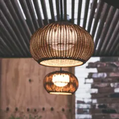 Dos lámparas de mimbre esféricas cuelgan bajo un techo de listones. La luz cálida que emiten crea un ambiente acogedor, con unos agradables lúmenes por m2.