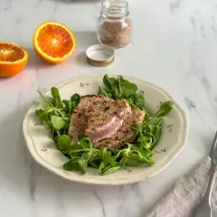 Tonno in padella con crosta di sesamo su letto di insalata fresca, accompagnato da spicchi d'arancia.