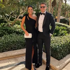 Ett par klädda för black tie dresscode, hon i en elegant svart klänning, han i smoking. De poserar glatt utomhus bland grönska.