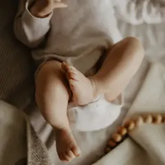 Malutkie nóżki i **szeroki brzuszek u noworodka** na miękkim kocyku. Obok drewniane koraliki i gryzak.