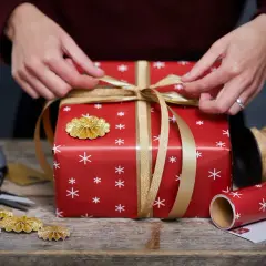 Här är några presentinslagningstips: en röd present med vita snöflingor, gyllene band och dekorationer.