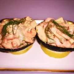 Zwei Avocadohälften gefüllt mit einem cremigen Krabbencocktail mit Avocado und Dill garniert, serviert auf Zitronenscheiben.