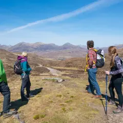 Four hikers enjoy a scenic view on Scotland hiking trips, with mountains stretching into the distance under a clear blue sky.