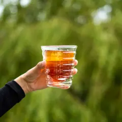 Dłoń trzyma szklankę z bursztynowym napojem, idealnym na orzeźwienie. Zastanawiasz się, jaka kawa do cold brew sprawdzi się najlepiej?