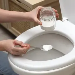 Une personne utilise une cuillère de bicarbonate de soude comme déboucheur canalisation maison pour un WC.