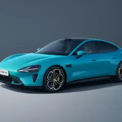 El elegante **Xiaomi SU7** azul turquesa, un sedán eléctrico con líneas aerodinámicas y techo negro, se exhibe sobre un fondo gris neutro.