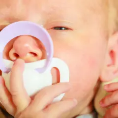Zbliżenie na twarz niemowlaka z fioletowym smoczkiem.