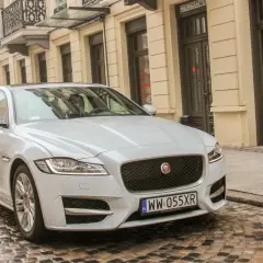 Biały Jaguar XF 3.0 Diesel na brukowanej ulicy przed kamienicą.
