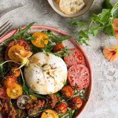 Ein bunter Tomaten Burrata Salat mit Rucola und essbaren Blüten.