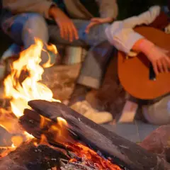 Przy ognisku siedzą ludzie, grają na gitarze i śpiewają piosenki do ogniska.