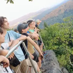 Grupa młodych ludzi podziwia widok z góry. To właśnie jest co to trekking – podróżowanie pieszo przez góry, odkrywanie piękna natury.