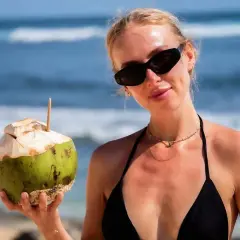 Kobieta w czarnym bikini trzyma kokosa na plaży. Idealne wakacje na Bali z orzeźwiającym napojem.
