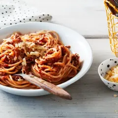 Ein Teller Spaghetti Bolognese, ein Klassiker unter den spaghetti rezepte, mit geriebenem Käse bestreut. Daneben eine Schale mit extra Käse.