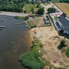 Słoneczny dzień nad zalewem Cedzyna. Ludzie odpoczywają na plaży, pływają i żeglują.