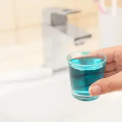 Mano tiene bicchierino con collutorio azzurro, ideale per l'igiene orale in gravidanza.