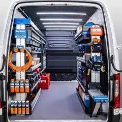 Interior de un autobús camperizado en España, organizado con estanterías y herramientas.
