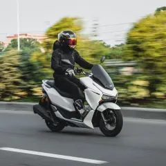 Hombre con casco y chaqueta negra conduce una moto 125 blanca por la autopista, demostrando que una moto 125 puede ir por autopista.