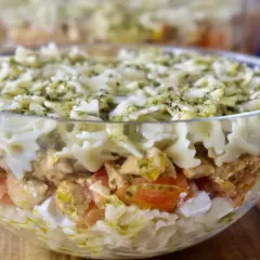 Pyszna, warstwowa sałatka z kurczakiem i makaronem farfalle, polana sosem pesto. Idealna na najlepsza sałatka z kurczakiem na imprezę!