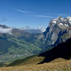 Panoramic view of a valley village nestled among green hills, with dramatic, snow-capped peaks of the Swiss Alps in the background. This scene exemplifies the best hikes in Swiss Alps.