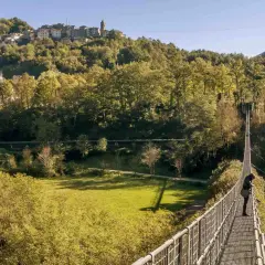Una persona osserva il panorama dal ponte sospeso delle Ferriere, con un borgo arroccato sulla collina sullo sfondo.