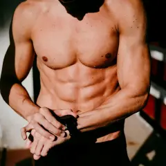 Ein Mann mit einem definierten Sixpack und nasser Haut blickt auf seine Sportuhr.