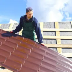 Un couvreur installe des tuiles en acier brun sur un toit. Ces tuiles garantissent une longue durée de vie bac acier.