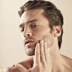 Un homme applique un soin sur sa barbe qui pique, sa main caresse sa joue.