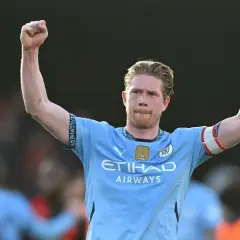 Kevin De Bruyne w jasnoniebieskiej koszulce z podniesionymi rękami, świętujący zwycięstwo.