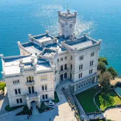 Zamek Miramare, biała perła nad turkusowym morzem, z wieżą górującą nad wodą.