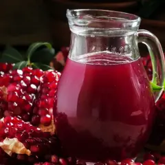 Sok z granatu w ciąży to zdrowy wybór. Na zdjęciu dzbanek z rubinowym sokiem i świeże granaty.