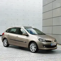 Beżowe Clio 3 kombi stoi na tle nowoczesnego budynku z betonową i metalową elewacją.