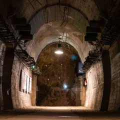 Wnętrze tunelu w Górach Sowich. Betonowe ściany, łukowe sklepienie i oświetlenie tworzą mroczny klimat.