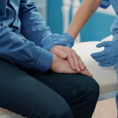 Pielęgniarka w niebieskich rękawiczkach pociesza pacjenta po operacji prostaty, który zmaga się z nietrzymaniem moczu.