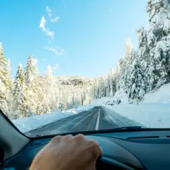 Conduciendo por una carretera nevada, rodeada de árboles cubiertos de blanco. Consejos para como conducir con nieve.