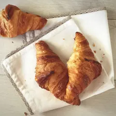 Trzy złociste rogaliki na białej serwetce z koronką, na drewnianym tle.