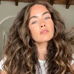Mujer con un espectacular pelo rizado castaño, con reflejos dorados, acariciando un mechón.