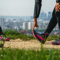 Zwei Läuferinnen dehnen sich auf einem Hügel mit Blick auf eine Stadt. Sie tragen schwarze Laufhosen und auffällige pink-schwarze Laufschuhe. Ein Zeichen für den Wiedereinstieg ins joggen nach Geburt.