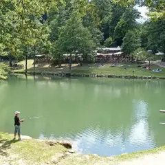 Un ragazzo pesca sul lago Pontini, mentre altre persone si rilassano sull'erba.