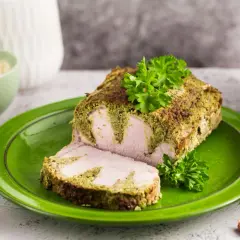 Schab pieczony w plastrach, z zieloną, ziołową panierką, podany na zielonym talerzu. Obok miseczka z majonezem i gałązki natki.